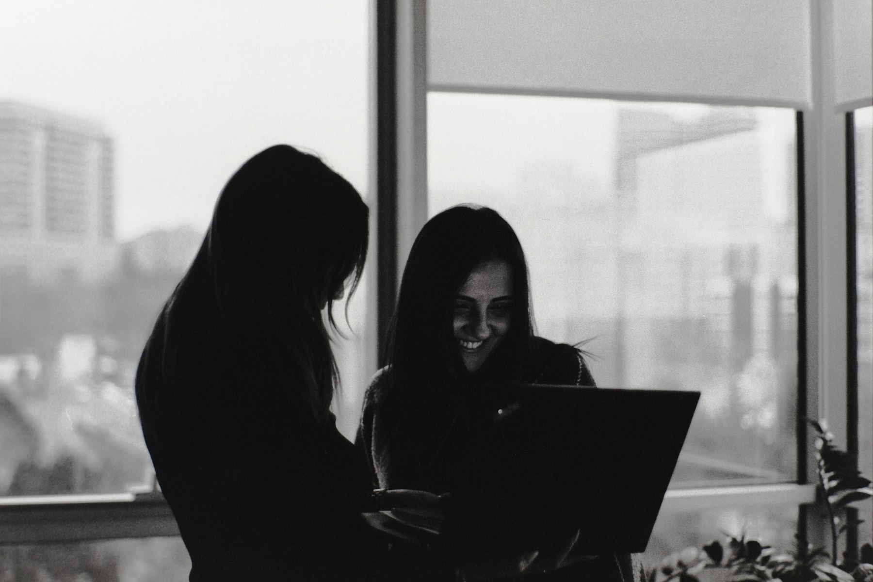 Two professionals reviewing a laptop beside a window